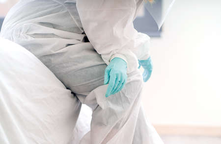 Detail of a doctor sitting in the hospital room wearing a safety suit and latex protective glovesの写真素材