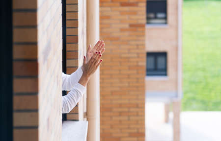 A woman claps from the window of her house in the quarantine of the state of alarm by the coronavirusの写真素材