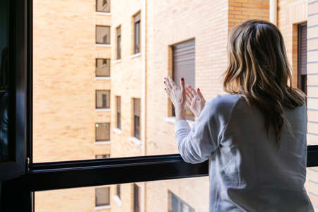 A woman claps from the window of her house in the quarantine of the state of alarm by the coronavirusの写真素材