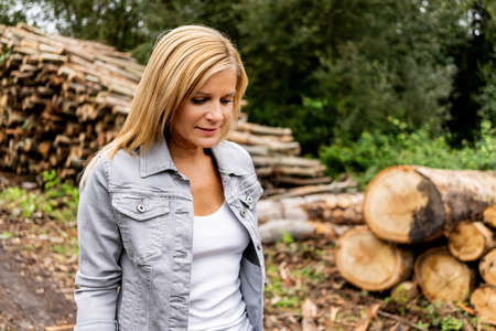 Portrait of a beautiful blonde woman in a denim jacket with wooden logs in the background