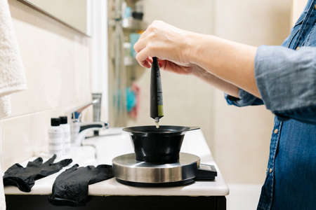 A woman prepares hair coloring products in her home bathroom.