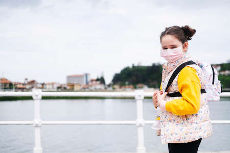 A girl with a mask by a promenade in a yellow sweater