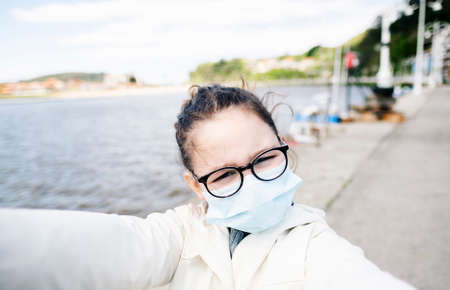 A girl with a mask in a fishing port in a town taking a selfieの写真素材