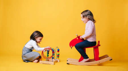 Two little girls play and learn with toys on a yellow isolated backgroundの写真素材
