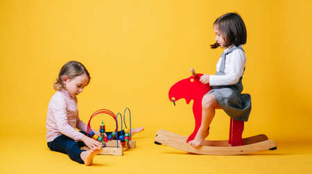 Two little girls play and learn with toys on a yellow isolated backgroundの写真素材