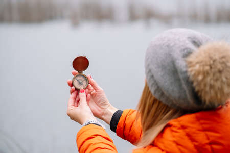 View of a tourist woman in a wool hat and orange coat in nature with a compass on a mountain lake in the backgroundの写真素材