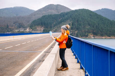 Front view of a female tourist with a map walking on a road with a green mountain landscape in the backgroundの写真素材
