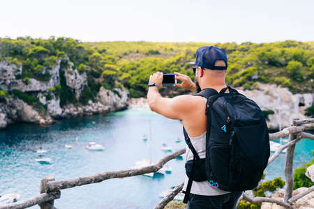 A tourist man with a backpack enjoys the views of a cove Macarella beachの写真素材