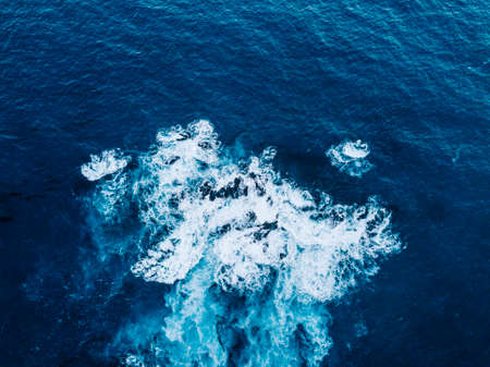 Aerial View of Waves Breaking on Rock. Light and dark blue water foaming whilst waves break to the shore. Deep Sea.の写真素材