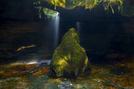 mossy stone with cave in the background with waterfallの写真素材