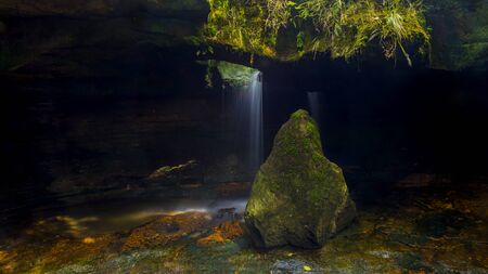 mossy stone with cave in the background with waterfallの写真素材