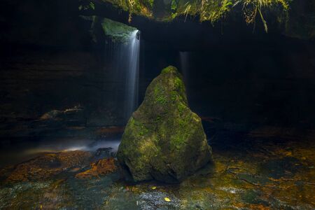 mossy stone with cave in the background with waterfallの写真素材