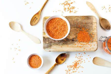 still life of red lentils in a white bowl on wood with a white background with wooden spoonsの写真素材
