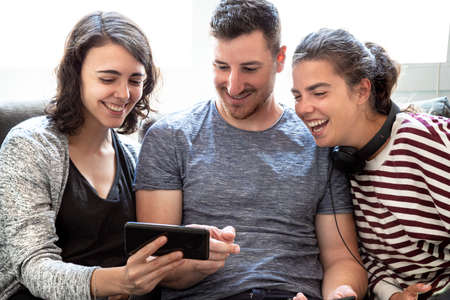 Group of friends having fun and laughing watching a video on the phone in a bright room. Concept...