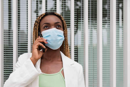 Portrait of young black woman talking with mobile phone wearing a face mask .. African american...