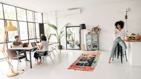 Young people working on laptop typing. Girl having coffee looking at cellphone. Big bright co working loft space. Co working concept. Working from home concept. Technology concept. Copy spaceの写真素材