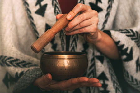 hands of a woman using a golden tibetan bowl in a meditation dressed with a handmade poncho. background with copy space. concept meditation. horizontal imageの写真素材