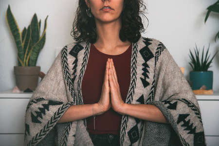 woman meditating with the palms of the hand joined on the chest dressed with a handmade ponchoの写真素材