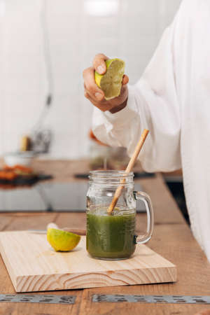 Close up. Woman's hand squeezing lime in green juice. Reusable bamboo straw. Kitchen counter top....
