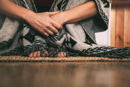 feet and hands of a woman sitting on a carpet on the floor wearing a handmade poncho. background with copy space. concept meditation. horizontal imageの写真素材