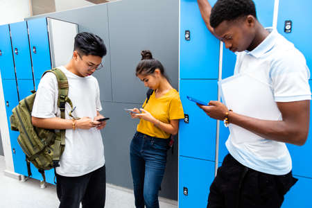 Group of multiracial teen students using their mobile phones in high school corridor. Back to school...