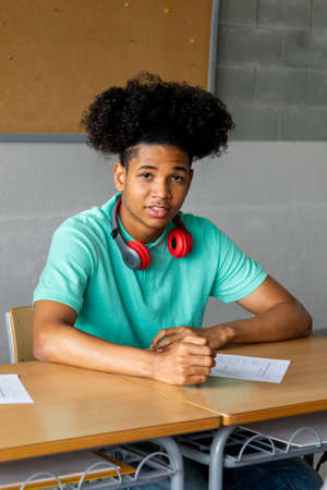 African american teen boy high school student sitting behind desk in classroom looking at camera. Education concept.の写真素材