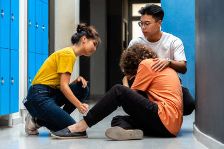 Two teen asian high school students comfort sad and depressed classmate victim of bullying in corridor. Bullying concept. Togetherness.の写真素材