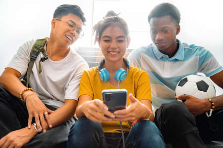 Multiracial group of teen high school classmates sit on stairs looking at teenage girl cell phone....