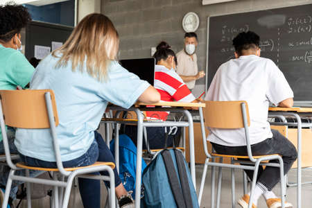 Mathematics class. Mature white male teacher wearing face mask in classroom with group of multiracial teen high school students. Education concept. Healthcare concept.の写真素材