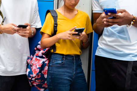 Close-up of teen high school students using mobile phone in school corridor. Social media concept. Cellphone addiction concept.の写真素材