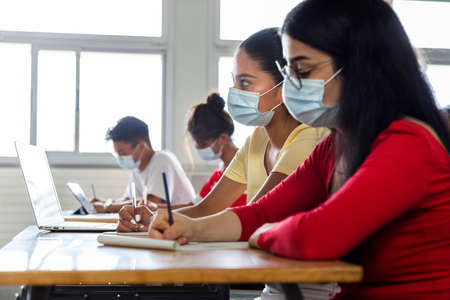 Multiracial group of teen high school students studying in class wearing protective face mask. Copy...