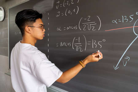Teen asian high school boy student solving maths exercise on blackboard with chalk. Education concept.の写真素材