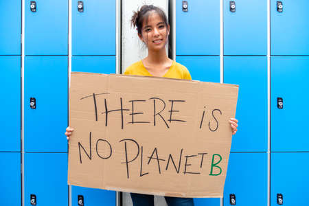 Teen asian high school girl student looking at camera carrying a vindictive "there is no planet b" placard. Sustainability concept.の写真素材