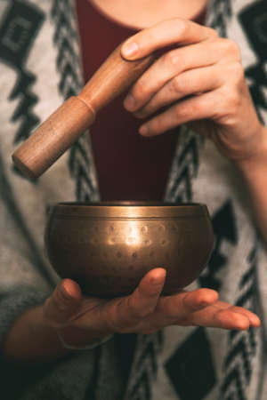 hands of a woman using a golden tibetan bowl in a meditation dressed with a handmade poncho. background with copy space. concept meditation. vertical imageの写真素材