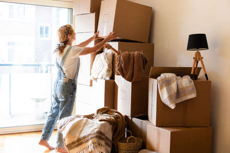 Mature adult blonde caucasian woman put cardboard box in a pile. Copy space. Moving in concept.
