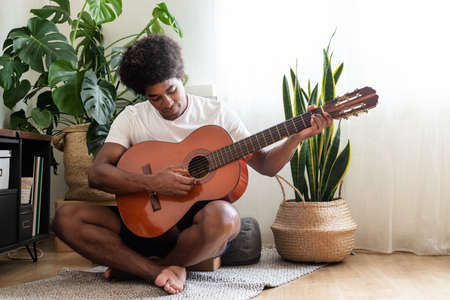 Young african american man plays acoustic guitar at home. Musical instrument practice concept....