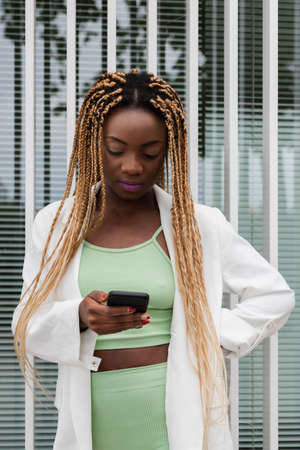 Young pretty black woman looking at cellphone. African american female with blond braids browsing through social media. Vertical image. Technology concept. Social media concept.の写真素材