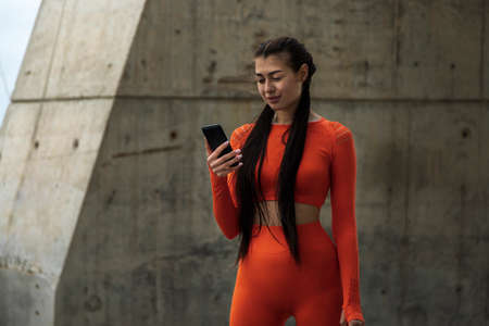Young caucasian athlete looking at her mobile phone. Woman in sportswear browsing through social media using her cellphone on gray concrete background. Fitness concept. Technology concept. Copy space.の写真素材