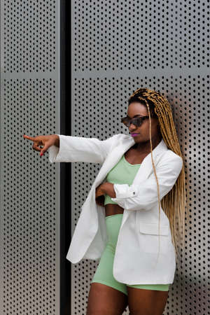 Young african american woman with long braids wearing sunglasses pointing index finger at someone....