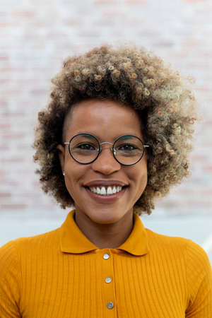 Headshot of smiling young african american woman with blond afro hair wearing glasses and yellow t-shirt.Vertical image.の写真素材