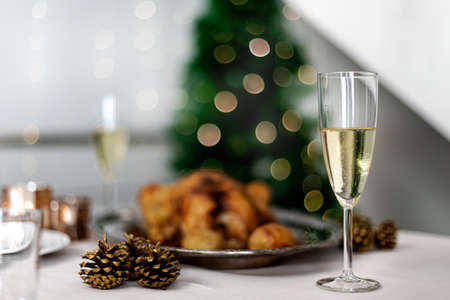 Christmas table setting with two glasses of champagne, roasted chicken anddecorations. Selective focus. Copy spaceの写真素材
