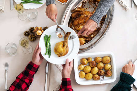 Top view of Christmas dinner table. Caucasian woman serving chicken to her son. Family holiday gathering.の写真素材