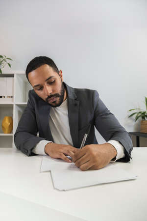 African american business man signs documents in his office. Latino male prepares before business meeting. Taking notes.の写真素材