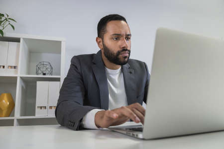 Young african american businessman working on laptop in home office. Focused entrepreneur typing on his computer.の写真素材