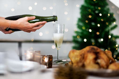 Hand serving glass of champagne on Christmas dinner table with blurred christmas tree on background. Selective focus.の写真素材