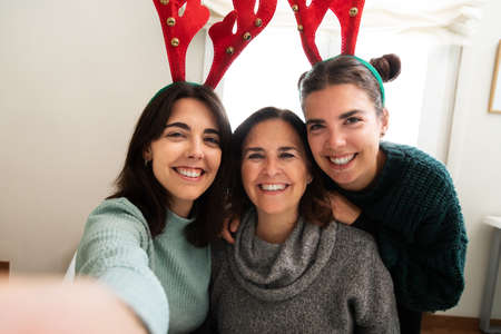 Happy and smiling caucasian mother and daughters taking a selfie during christmas family party. Felt reindeer antlers.の写真素材
