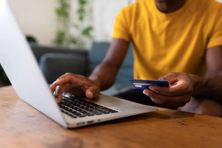 Unrecognisable African American man using laptop and credit card to buy things online.