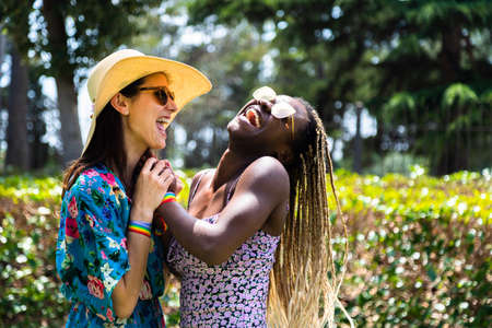 Happy multiracial couple of gay women laugh together in a hot summer day in blurred background. Copy space.の写真素材