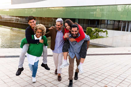 Multiracial group of friends have fun together in the city. Friends give piggyback rides to other...