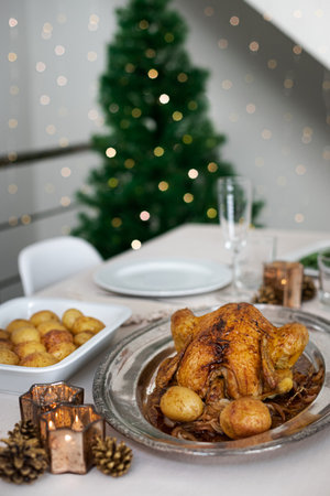 Christmas dinner minimalist table setting with roasted chicken and christmas tree on background.の写真素材